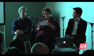 Three people sit on a panel discussion stage with microphones. A woman in the center reads from papers, flanked by two men. A laptop with an Apple logo is open on the table. The room is dimly lit, and an ICA logo is visible in the corner.